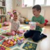 Jucării squishy Doi copii pe covor cu găletușa de jucării squishy, fetița ridicând un iepuraș roz