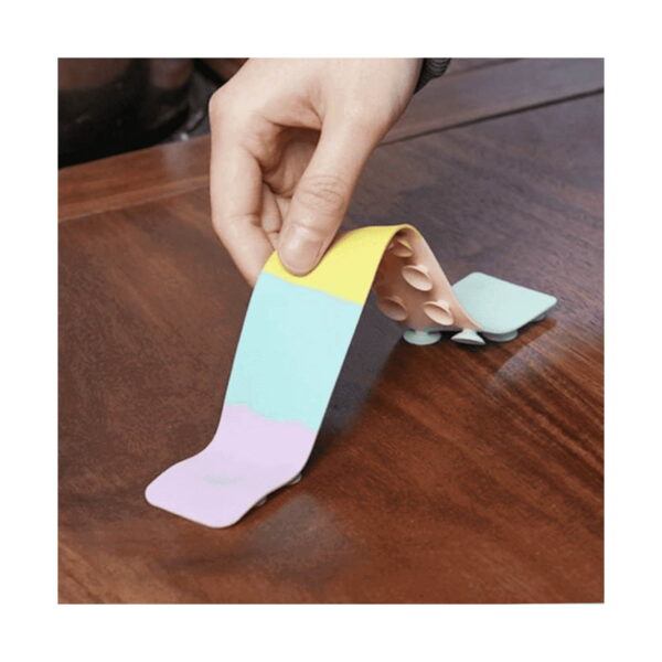 Benzi Fidget Squidopops XL, o mână de adult dezlipește de pe o masă de lemn o bandă Fidget cu segmente galben, mentă și lila