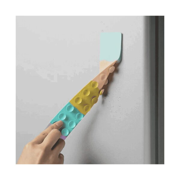 Benzi Fidget Squidopops XL, o mână apasă pe un perete gri o bandă Fidget pastel cu ventuze