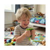 Bob de fasole Fidget, băiat care râde, într-o cameră de copii, ținând în mâini păstaia verde fidget