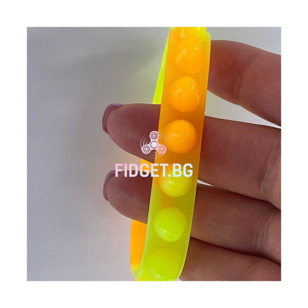 bratari-luminoase-fidget-fucsia-si-portocalii-detaliu Brățări luminoase Fidget, prim-plan cu o brățară translucidă portocaliu-galben, ținută între degete