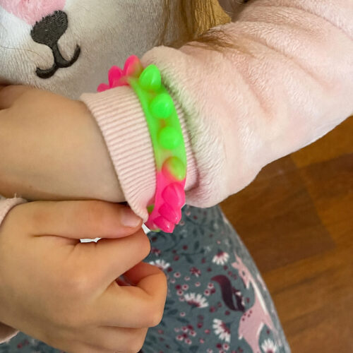 Brățări luminoase Fidget, încheietura unui copil cu o brățară fidget fucsia cu bile verzi, pusă peste mâneca unei bluze roz