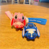 Breloc Lilo & Stitch, brelocurile Stitch roz și albastru pe o masă de lemn, cu curelele imprimate alături