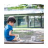 cuburi-constructie-lemn-castel-montessori-utilizare-3 Cuburi construcție, băiat în tricou albastru stă pe jos afară și se joacă cu piese de lemn, lângă cutia setului