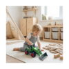 Excavator de jucărie, un băiețel blond se joacă pe covor, într-o cameră de copii, cu tractorul verde cu încărcător