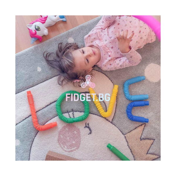 Fidget Pop Tubes XL, fetiță culcată pe covor lângă cuvântul LOVE format din tuburi colorate