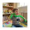 fidget-pop-tubes-xl-roz-utilizare Fidget Pop Tubes XL, băiat în tricou în dungi ține un tub verde întins în spatele gâtului, într-o cameră cu rafturi de cărți