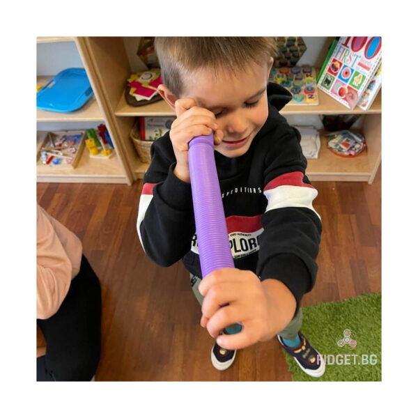 fidget-pop-tubes-xl-roz-utilizare-3 Fidget Pop Tubes XL, băiat care privește printr-un tub mov ținut vertical, într-o cameră de joacă