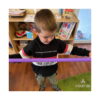 fidget-pop-tubes-xl-roz-utilizare-4 Fidget Pop Tubes XL, băiat care întinde un tub mov-roz în jurul corpului, în fața unui raft cu jucării