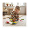 forme-de-puzzle-din-lemn-montessori-utilizare-2 Forme de puzzle din lemn Montessori, copil zâmbind, așezat pe covor, potrivind piese colorate pe placa