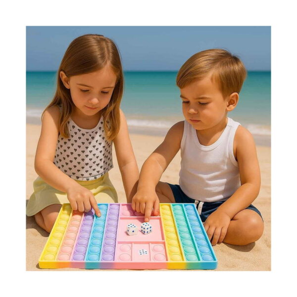 Joc Pop It cu zaruri, o fetiță și un băiat, pe plajă lângă mare, apasă bulele tablei pastel cu două zaruri în mijloc