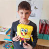 Jucărie de pluș SpongeBob, băiat în bluză gri închis, într-o sală de clasă