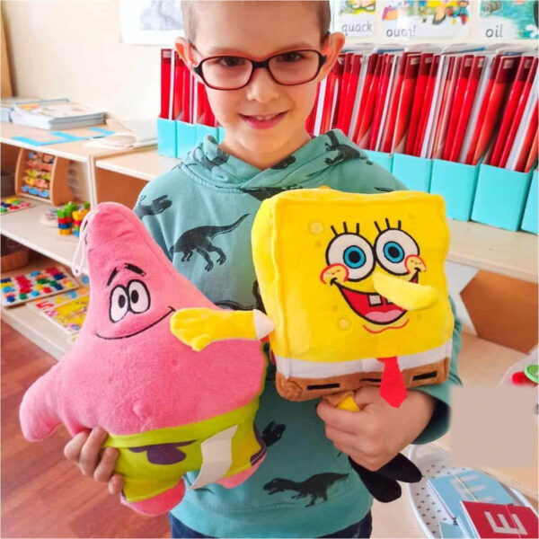 Jucărie de pluș SpongeBob, băiat cu ochelari ținând în brațe două jucării: steaua roz Patrick în stânga și SpongeBob