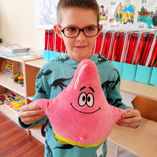 Jucărie de pluș SpongeBob, băiat cu ochelari, într-o sală de clasă, ținând în brațe jucăria roz Patrick