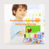 kit-de-pictura-cu-nisip-colorat-12-planse-utilizare Kit de pictură cu nisip colorat, un băiat cu șorț zâmbește în fundal, iar în prim-plan sunt cutia verde cu rățușcă