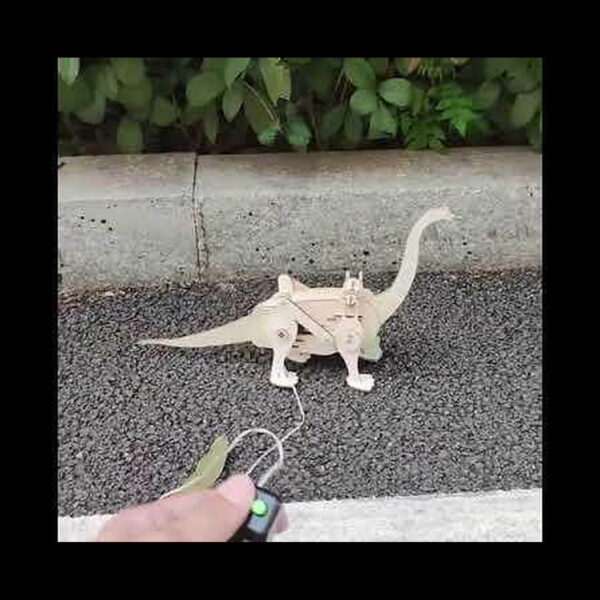 kit-stem-brachiosaurus-din-lemn-utilizare Kit STEM Brachiosaurus din lemn, o mână ține telecomanda, iar dinozaurul din lemn merge pe un trotuar cu pietriș