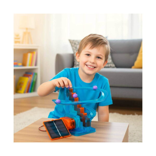 kit-stem-tobogan-solar-2 Kit STEM Tobogan solar, băiat în cameră, la o măsuță, atinge toboganul solar cu bile mov; panoul solar este alături