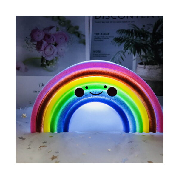 lampa-de-veghe-3d-curcubeu-iluminat Lampă de veghe 3D curcubeu, curcubeu aprinsă, pe o suprafață albă cu stele, în fața unor flori