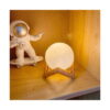 lampa-de-veghe-3d-luna-utilizare-7 Lampă de veghe 3D lună, lună aprinsă pe suport din lemn, pe un raft din lemn, lângă o figurină de astronaut pe skateboard