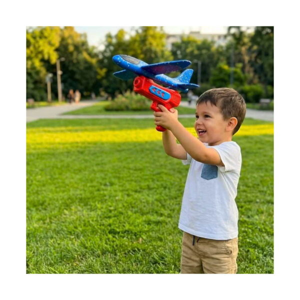 Lansator de avion Unlimit, băiat într-un parc, care ține lansatorul roșu cu avionul albastru montat