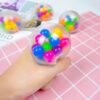 minge-squishy-3 Minge squishy, mână care strânge mingea squishy transparentă cu bile colorate, pe un fundal roz cu carouri