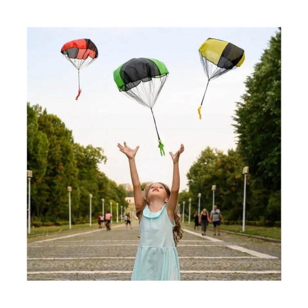 Parașută de joacă pentru copii, fetiță cu brațele ridicate spre trei parașute de jucărie cu figurine, pe aleea unui parc