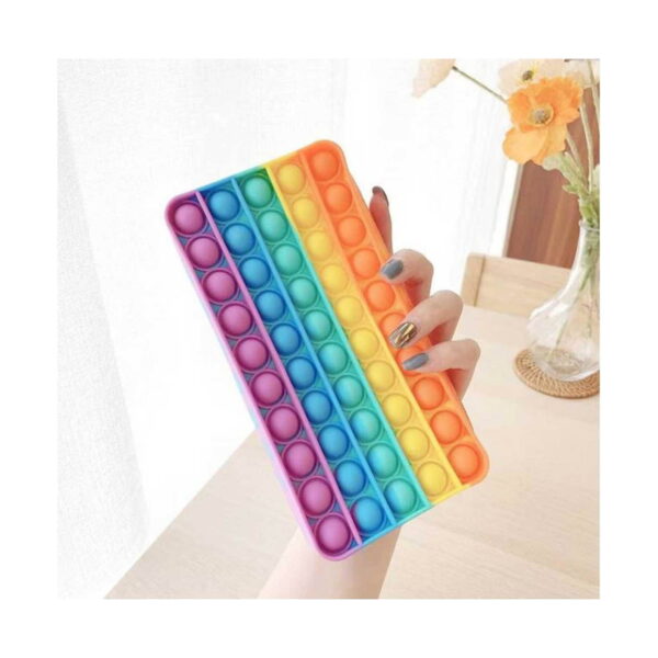 penar-pop-it-curcubeu-dimensiuni Penar Pop It curcubeu, o mână ține penarul curcubeu într-o cameră luminoasă, cu flori portocalii în fundal