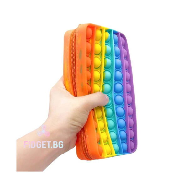 penar-pop-it-curcubeu-utilizare Penar Pop It curcubeu, o mână ține penarul curcubeu, cu fermoarul portocaliu și grosimea compartimentului vizibile