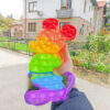Pop It colorat Mickey Mouse 30x20, jucăria ținută în mână pe o stradă, cu case și gard în fundal; nu apar cote