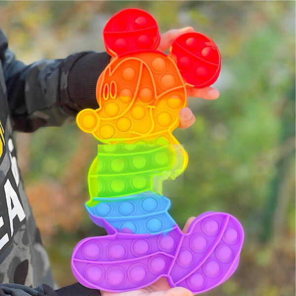 Pop It colorat Mickey Mouse 30x20, jucăria ținută în mână în aer liber, cu vegetație verde neclară în fundal; nu apar cote