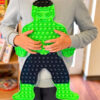 Pop It Hulk, un copil în bluză gri ține în brațe jucăria Pop It verde în formă de personaj musculos, într-o cameră