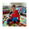 Pop It Spider-Man, băiețel zâmbind pe covorul din camera lui, ținând jucăria Spider-Man cu ambele mâini
