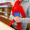 Pop It Spider-Man, copil în hanorac gri care ține jucăria Spider-Man în fața corpului, într-o sală cu rafturi de cărți