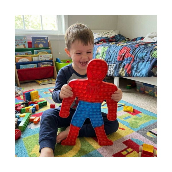Pop It Spider-Man, băiețel zâmbind pe covorul din camera lui, ținând jucăria Spider-Man cu ambele mâini