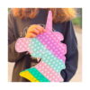 Pop It unicorn, prim-plan cu unicornul Pop It ținut în fața unui pulover bleumarin, care arată mărimea jucăriei