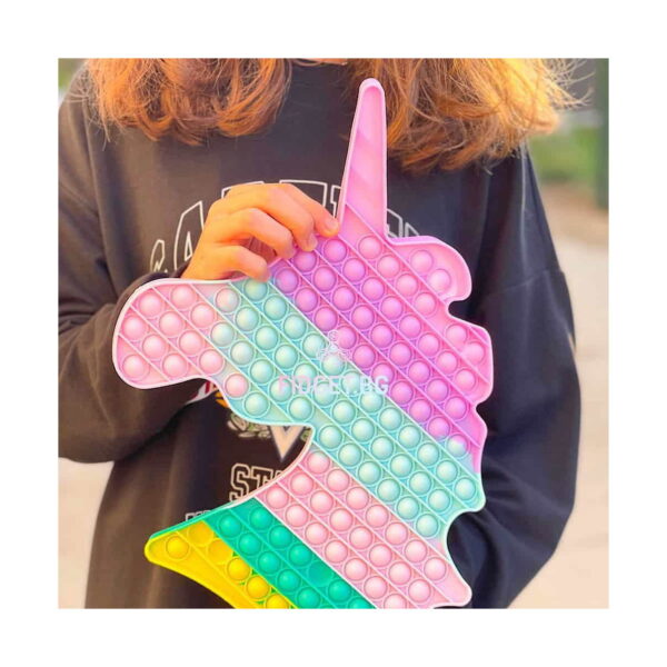 Pop It unicorn, prim-plan cu unicornul Pop It ținut în fața unui pulover bleumarin, care arată mărimea jucăriei