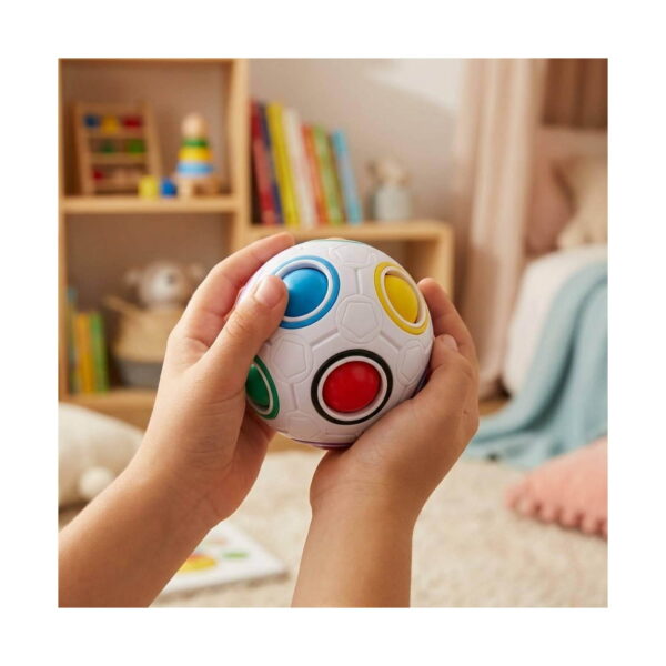 Puzzle Rubik Minge, mâinile unui copil țin mingea într-o cameră cu rafturi și cărți în fundal
