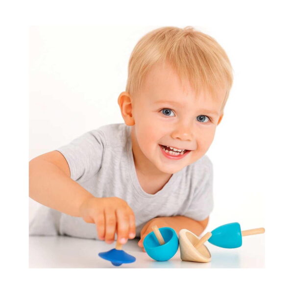 set-4-spinner-din-lemn-utilizare Set 4 Spinner din lemn, băiat blond zâmbitor atinge titirezele așezate pe o suprafață albă