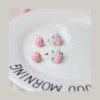 Set creativ Hello Kitty 3 în 1, prim-plan cu doi cercei cu fața albă Hello Kitty, fundiță roz și bilă roz-alb în dungi