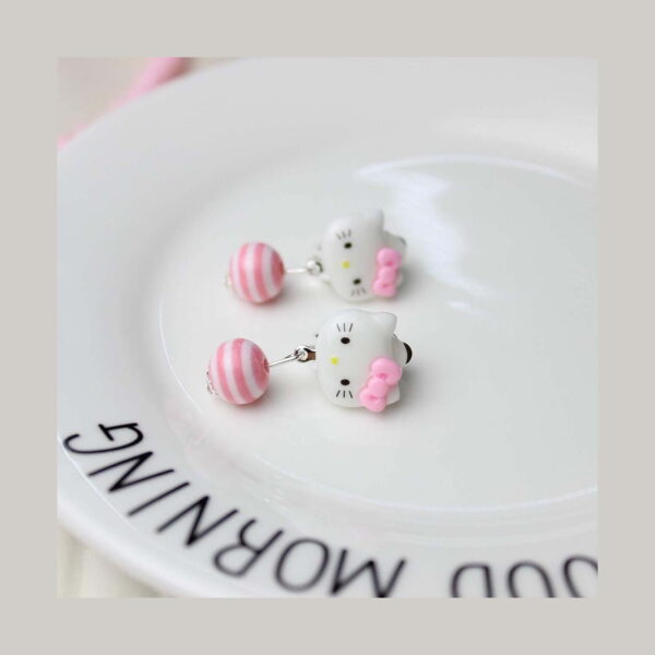 Set creativ Hello Kitty 3 în 1, prim-plan cu doi cercei cu fața albă Hello Kitty, fundiță roz și bilă roz-alb în dungi