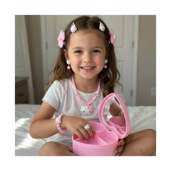 Set creativ Hello Kitty 3 în 1: Pop It, fetiță pe pat purtând colier, brățară, inel, cercei și agrafe roz