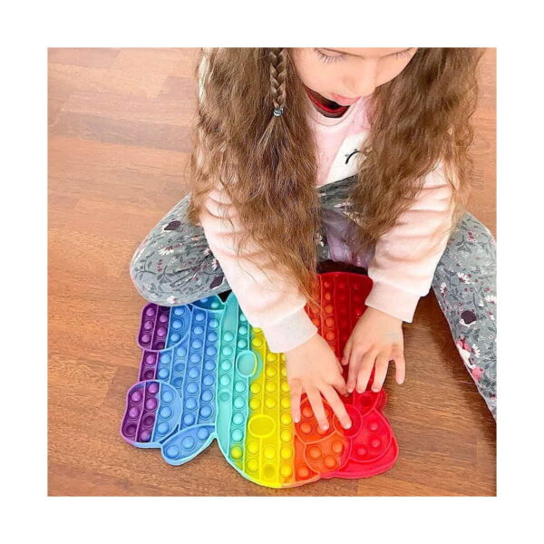 Set creativ Hello Kitty 3 în 1: Pop It, fetiță pe podea care apasă cu ambele mâini bulele unui Pop It Hello Kitty curcubeu.