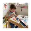 Set creativ Paw Patrol cu 4 activități, băiat la o măsuță din lemn pictând o figurină Marshall din gips; pe masă vopsele