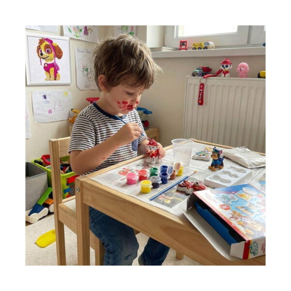 Set creativ Paw Patrol cu 4 activități, băiat la o măsuță din lemn pictând o figurină Marshall din gips; pe masă vopsele