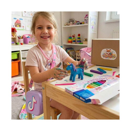 Set Creativ Tik Tok, fetiță la o masă, cu un unicorn modelat din plastilină albastră, batoane de plastilină verzi