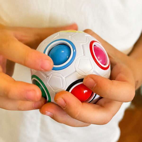 set-de-2-mingi-rubik-utilizare-2 Set de 2 mingi Rubik, prim-plan cu degetele unui copil care apasă bilele colorate din locașurile mingii Rubik albe