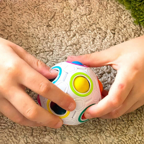 set-de-2-mingi-rubik-utilizare-3 Set de 2 mingi Rubik, mâinile unui copil care apasă bilele mingii Rubik albe, deasupra unui covor bej