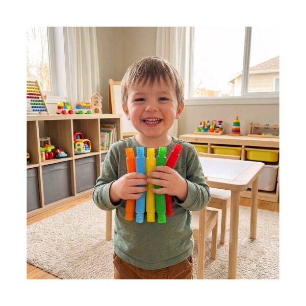 set-de-5-fidget-pop-tubes-mici-utilizare Set de 5 Fidget Pop Tubes mici, băiețel zâmbitor într-o cameră de joacă, ținând în mâini cinci tuburi mici, colorate
