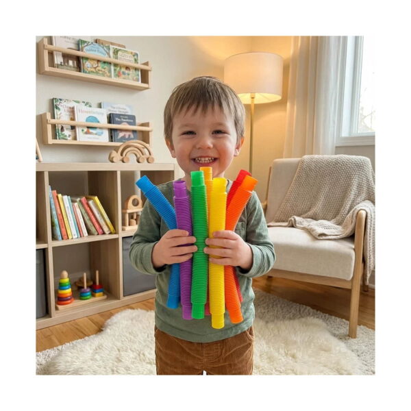 Set de 7 Pop Tubes mari, băiețel zâmbitor în sufragerie, ținând în brațe mai multe tuburi Pop Tube mari, colorate