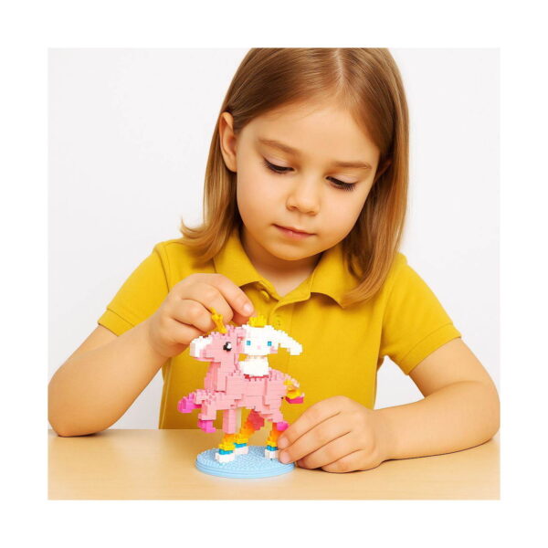 set-de-constructie-3d-hello-kitty-utilizare Set de construcție 3D Hello Kitty, fetiță la masă, pe fundal alb, asamblând unicornul roz din micro cărămizi